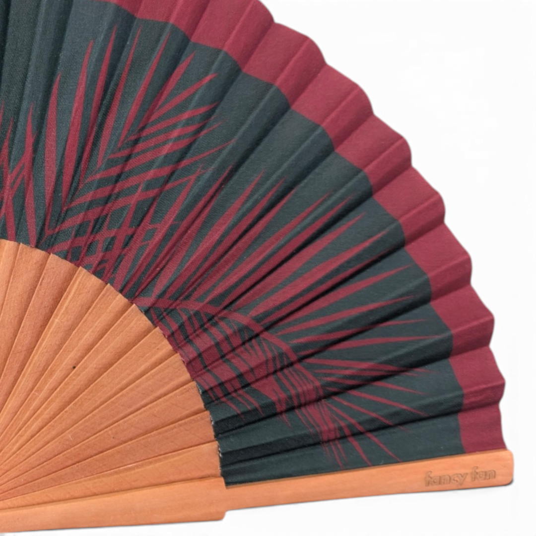 LE BAZAR INOUI PALM LEAFS Fächer mit dunkelgrünem und weinrotem Palmenblatt-Print auf einem hellen Holzrahmen.