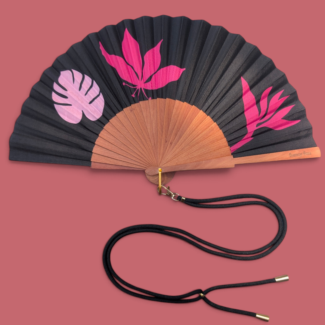 LE BAZAR INOUI BLOSSOMS Handfächer mit schwarzem Stoff, pinkem Blumenmuster und braunem Holzrahmen mit Trageband.