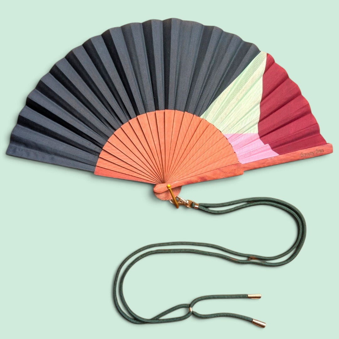 LE BAZAR INOUI SOLID STRIPES Fächer mit Holzrahmen, schwarz-rotem Stoff und grünem Umhängeband auf hellgrünem Grund.