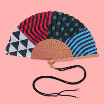 LE BAZAR INOUI RHAPSODY II Handfächer mit buntem geometrischem Muster, Holzrahmen und schwarzem Umhängeband.