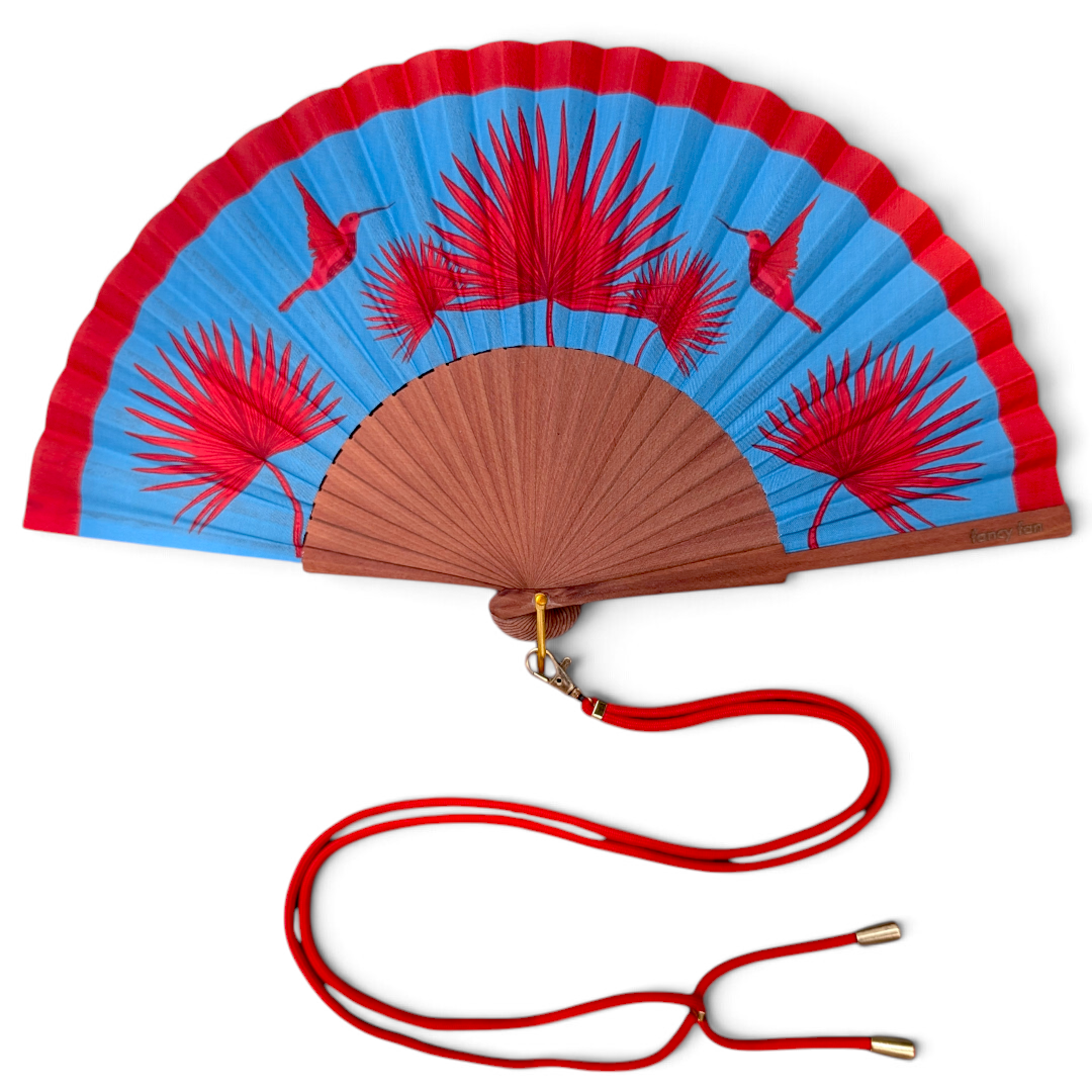 LE BAZAR INOUI RUBY BIRD Faltfächer aus Holz und Stoff mit Kolibri-Print, blauem Hintergrund und rotem Umhängeband.